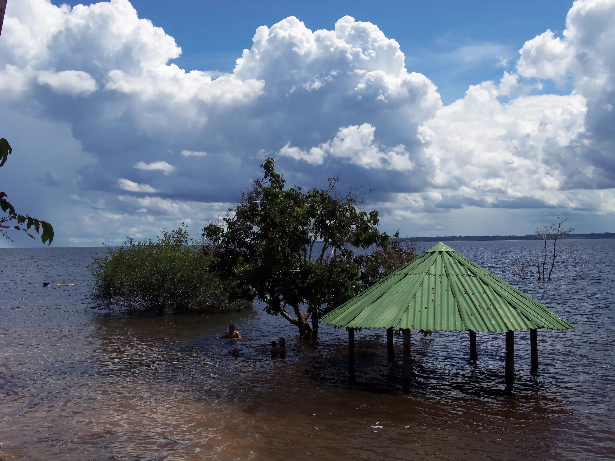 Quiosque de telhado verde com a água do rio Negro na altura das colunas e nuvens grandes no céu