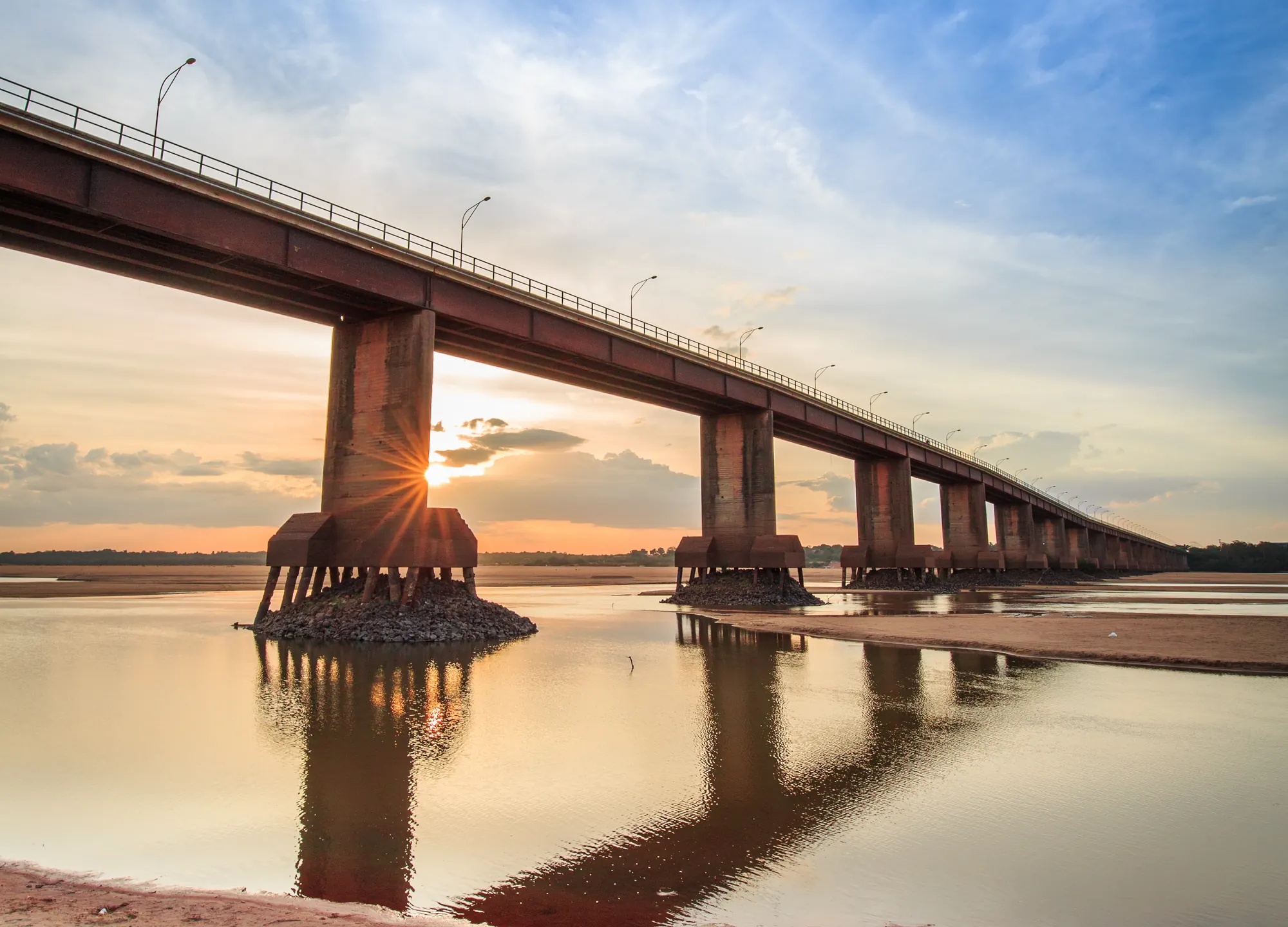 Ponte dos Macuxis, em Boa Vista, com o sol se pondo entre os pilares sobre o rio Branco