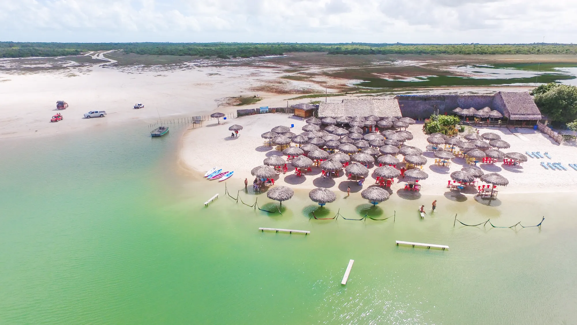 Vista aérea de uma lagoa de água verde em Jericoacoara, com guarda-sóis de palha na areia