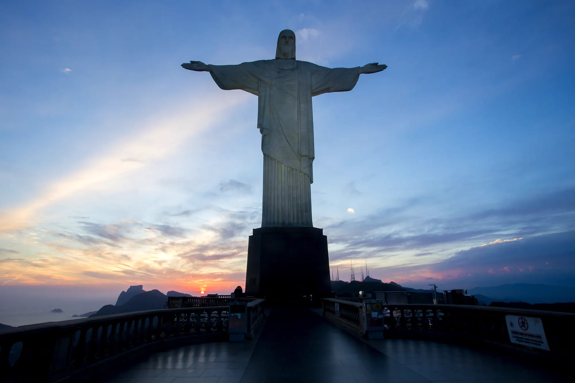 Cristo Redentor em silhueta contra um céu azul e alaranjado ao entardecer